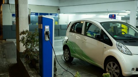 Carsharing electric car is charging in the indoor parking. The indicator on the station flashes green. Camera zoom moves on object