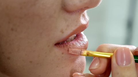 Closeup view of a professional makeup artist applying lipstick on model's lips working in beauty fashion industry. Closeup view of an artist's hand using special brush. slow motion