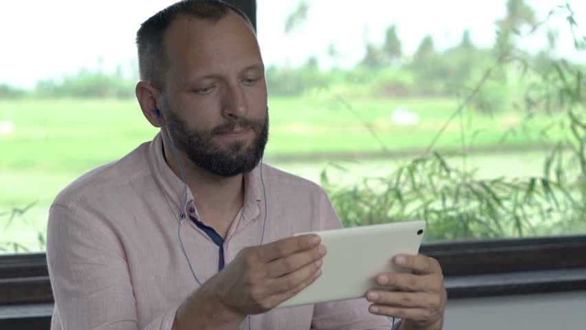 Happy man watching movie on tablet and drinking beverage at home
