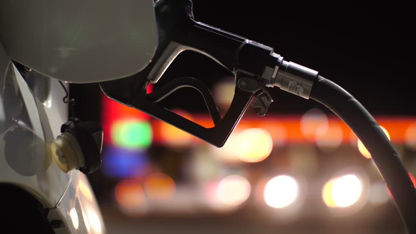 Fuel nozzle inserted in car's gas tank as it's being refueled at gas station pump at night. Closeup, shallow DOF. 4K UHD. Royalty-Free Stock Footage #32924410