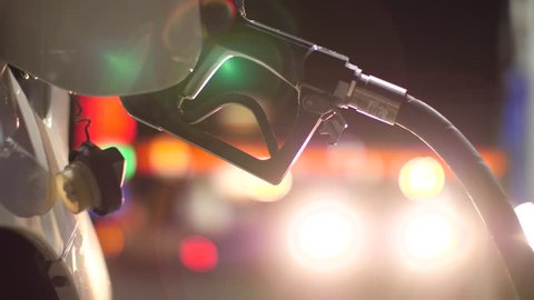 Fuel nozzle inserted in car's gas tank as it's being refueled at gas station pump at night. Closeup, shallow DOF. 4K UHD.