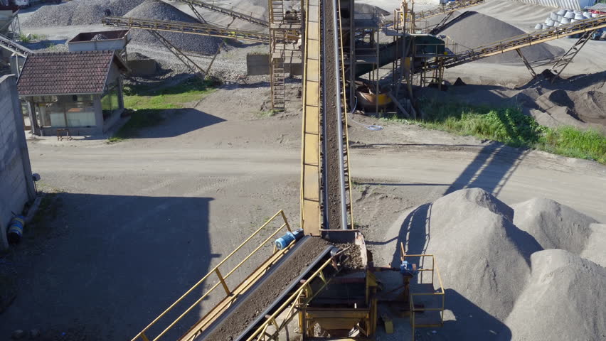 Aerial view, camera tracking conveyor belt that transporting rocks and soil while dropping on heap, stone crusher machine, mixer truck leaving, plant for sand and gravel production, building industry Royalty-Free Stock Footage #32924842