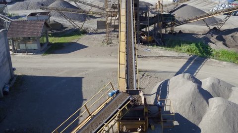 Aerial view, camera tracking conveyor belt that transporting rocks and soil while dropping on heap, stone crusher machine, mixer truck leaving, plant for sand and gravel production, building industry