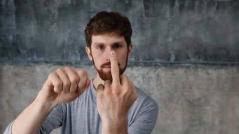 Portrait of a young Red-haired bearded man showing middle finger gesturing fuck. White man makes fuck gesture with a hand on light gray background. Guy slowly showing middle finger sign fuck off
