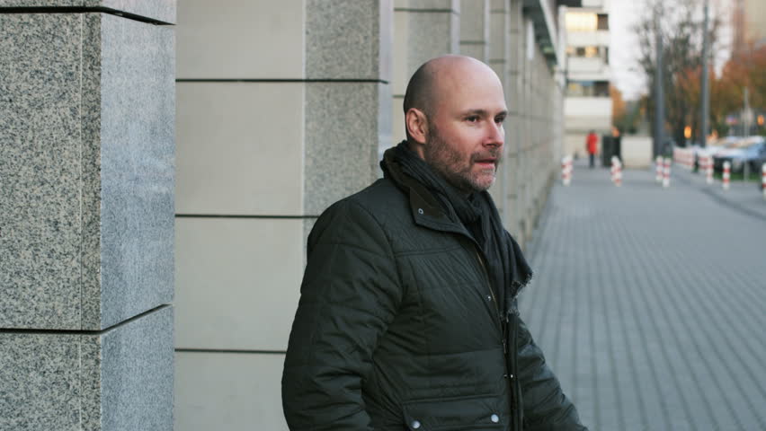 Bald Bearded Man Putting on a Winter Hat in the Street