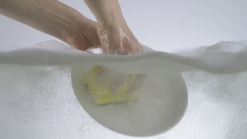 Slow Motion Shot Of Hands Washing A Ceramic Plate Using Detergent And Sponge. 