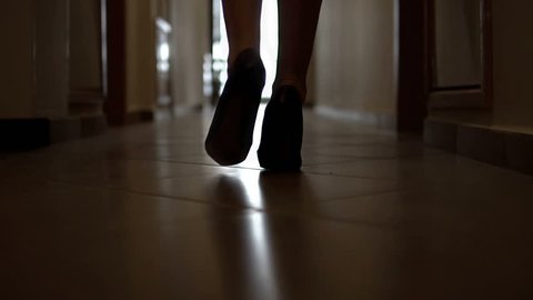 Silhouette of a fashion model female walking along a dark corridor in high hills shoes, SLOW MOTION