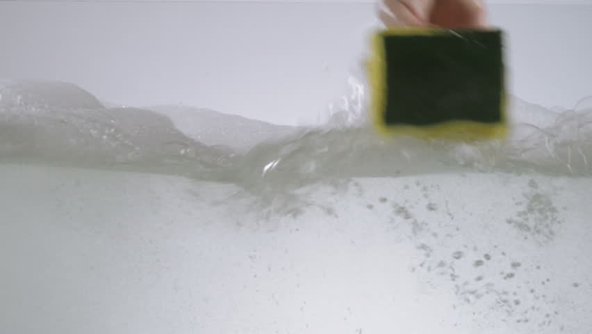 Hands washing a glass fish tank using washing detergent and sponge. 