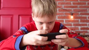 Closeup portrait of cute funny little child playing computer games on smartphone at Christmas holiday time. Xmas time. Wide angle real time full hd video footage.