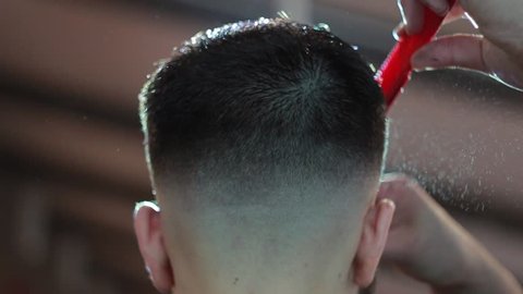Barber makes a male haircut with a professional scissors and a comb in a barbershop on light background, close-up.