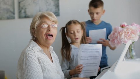 Grandmother with grandchildren playing piano and singing songs.