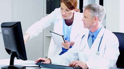 Caucasian Male medical consultant with young female doctor updating patient computer records using tablet shot on RED EPIC