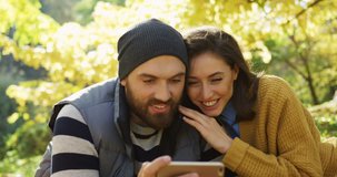 Close up of young smiling couple video chatting on the smart phone and hugging in the beautiful park in fall. Sunny weather. Outdoor