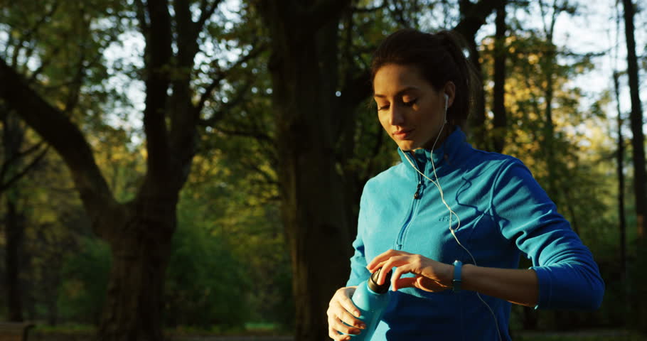 Attractive sporty woman drinking water from thermos after jogging in the park on sunset. Outdoors