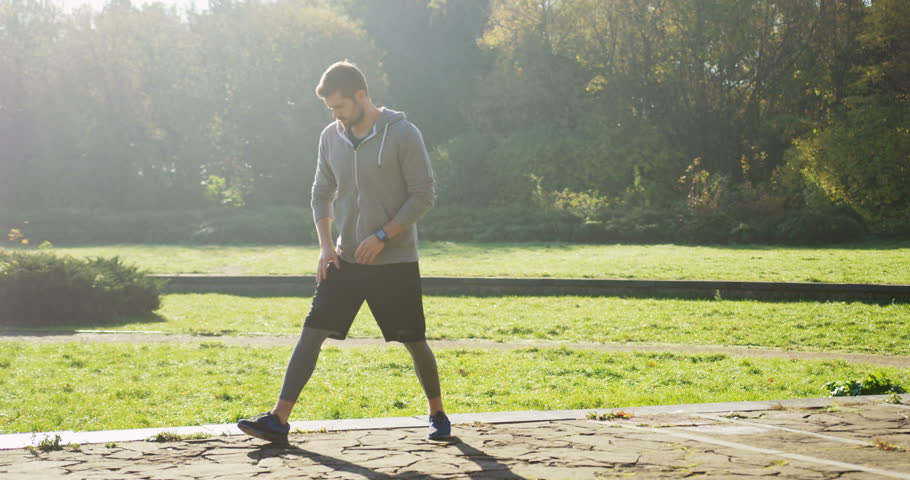 Young attractive man stretching his legs early in the morning in the beautiful green park. Outdoor