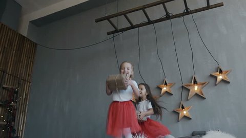 The two little sisters of the twin actively have fun at the bed of their parents. Children dressed in identical red skirts, jump on the bed with Christmas gifts in their hands slow motion