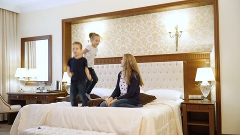 Scene Shows Young family Jumping on Bed in Room. Mom, Dad and children of European Appearance. Concept of Happy Family Life, Success, Entertainment, Advertising Hotels or Bed Linen