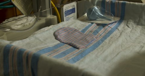 A baby crib lies empty with a single hat lying flat with some blankets