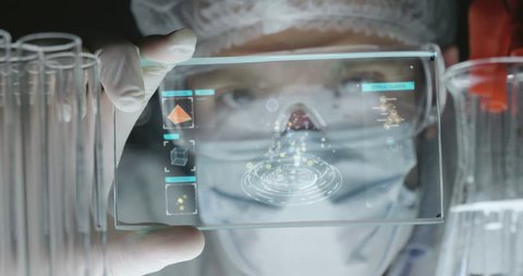A futuristic physician, a surgeon, examines a technological digital holographic plate, a medical mask, a cap, brown eyes. Concept: futuristic medicine, new technologies, doctors, laboratory, future.