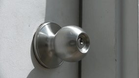 Clip of hands trying to unlock door knob with multiple keys only to find the right one and open the white door.