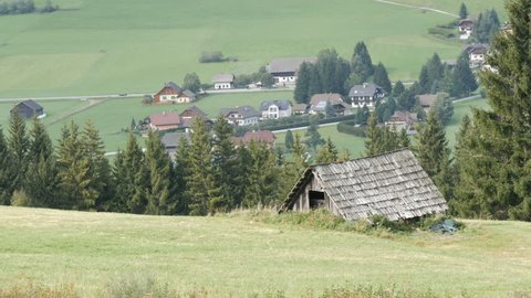 A cozy very old vintage wooden house in the Austrian Alps on a hill with green grass on the background of new modern houses, Old rural country wooden house in village