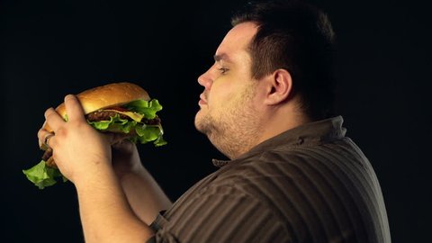 Fat man eating hamberger fast food . Breakfast for overweight person . Junk meal leads to obesity. Person regularly overeats concept .