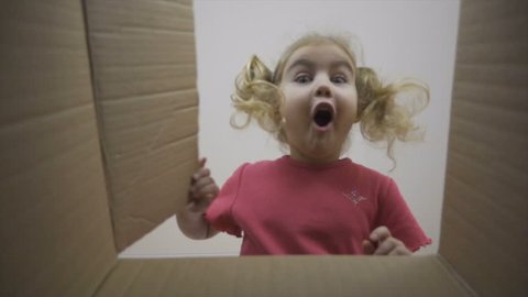 A little girl looks in the box, is surprised and happy to receive a surprise. The child opened a box with a gift.Slow Motion