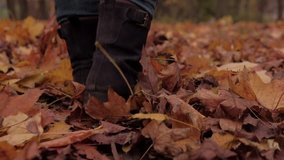 Camera follows behind boots of woman walking through autumn leaves. Shot in real time on a gimbal