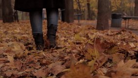 Camera follows behind boots of woman walking through autumn leaves. Shot in slow motion
