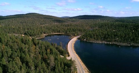 Arctic road, Cinema 4k aerial view over a asphalt road between, pine tree forest, a lake and tunturi fjeld mountains, on a sunny autumn day, near Inari, in Lapland, Finland