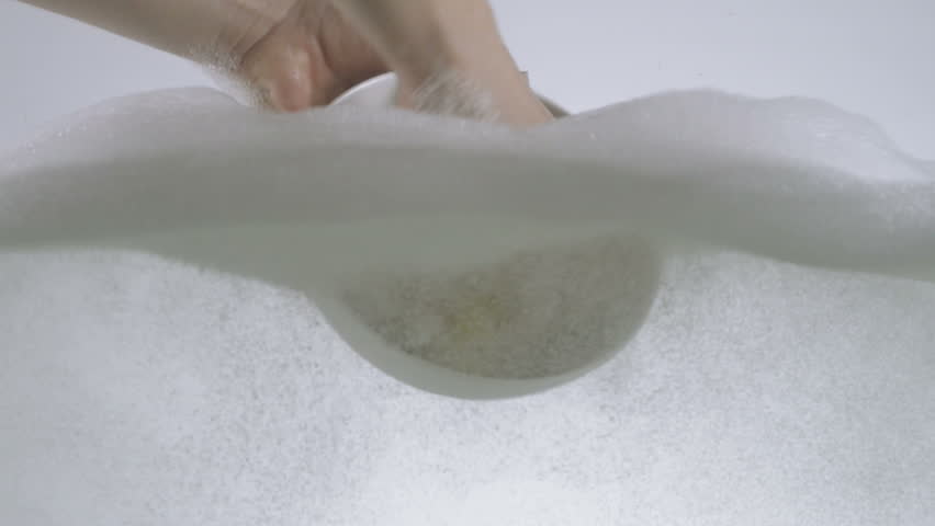 Hands washing a small serving bowl using washing detergent and sponge. 
