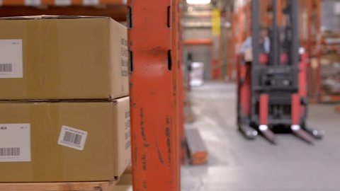 A forklift passes by boxes of inventory in a large distribution center.