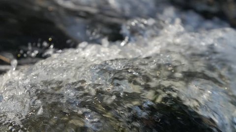 Close up of water stream with white and transparent bubbles. Slow motion.