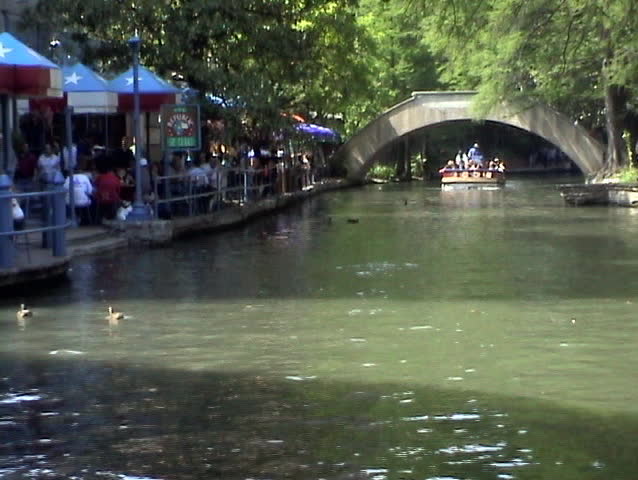 Video of the San Antonio Texas Riverwalk. Tourist barge near restaurant area. Tourist and passengers. Walk, business, umbrellas and bridge. Vacation. 