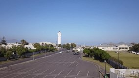 4K high quality aerial video scenic sunny morning view of historical lighthouse and Table Mountain at the background near beach at sea shore in Milnerton, Cape Town, South Africa