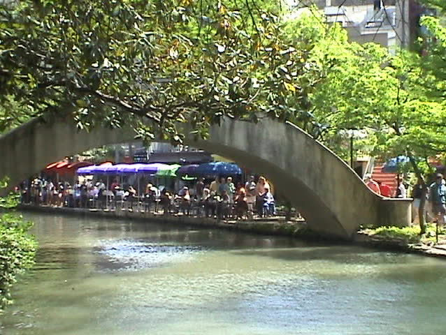 Video of the San Antonio Texas Riverwalk. Tourist barge near restaurant and foot bridge. Tourist and passengers. Walk, business, umbrellas and bridge. Vacation. 