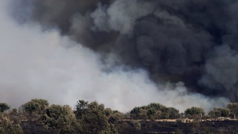 Long shot of fire in the horizon with black and white smoke