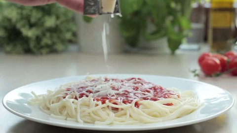 A chef grates fresh cheese onto pasta with tomato sauce, tracking shot