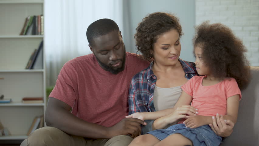 Mother tickling and amusing her little daughter, family sitting on couch