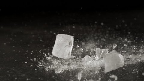 Ice cube bouncing and crashing on graphite sheet with dark background table top in slow motion