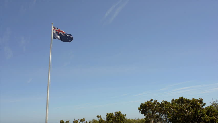 An Australian flag flying and flapping in the wind, with lots of blue sky and