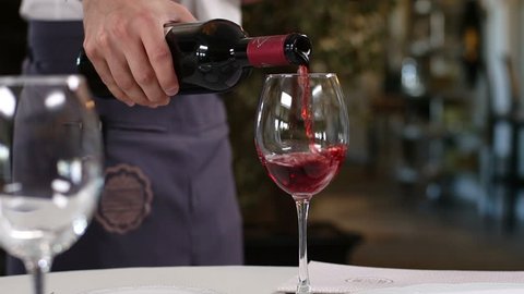 macro skilled waiter in uniform serves visitors pouring tasty red wine into cleaned wineglasses