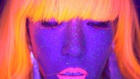 Closeup woman face and torso with fluorescent make up in orange wig, creative makeup look great for nightclubs. Halloween party, shows and music concept - slow motion video