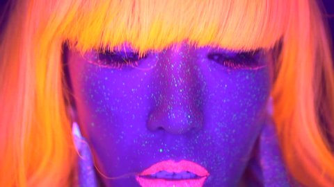 Closeup woman face and torso with fluorescent make up in orange wig, creative makeup look great for nightclubs. Halloween party, shows and music concept - slow motion video