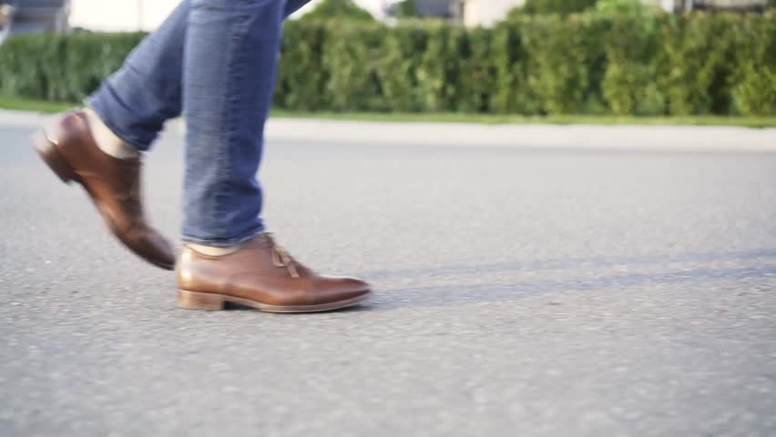 Unrecognizable man wearing blue jeans and brown leather shoes is walking in the street with no traffic. Side view. Tracking real time establishing shot Royalty-Free Stock Footage #33028747