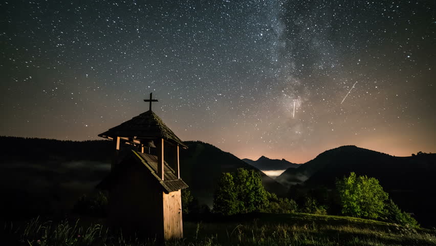 Stars with milky way galaxy moving over wooden belfry in mountains and foggy valley rural country. Dolly shot time lapse starry night sky
