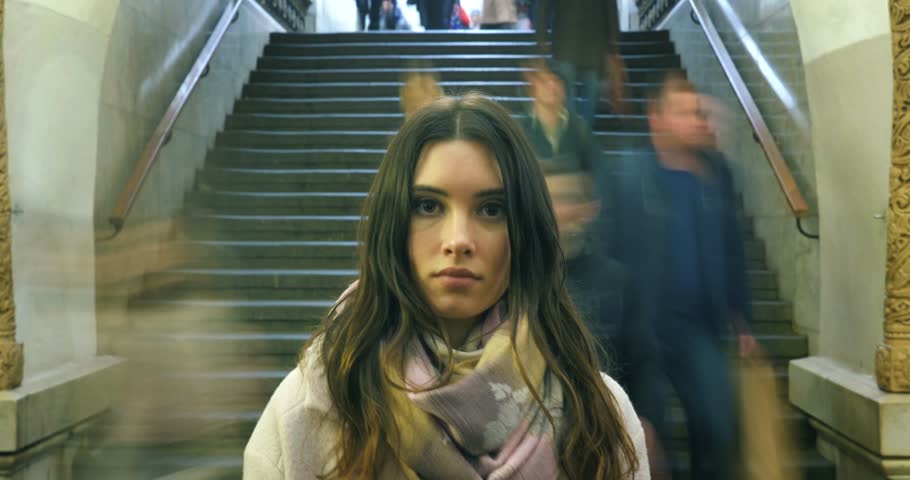 Beautiful young woman looking at camera, closeup. Moving crowd of people blurred in motion in background. 4K UHD timelapse. Royalty-Free Stock Footage #33032461
