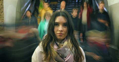 Beautiful young woman looking at camera, closeup. Moving crowd of people blurred in motion in background. 4K UHD timelapse.