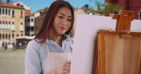 Attractive woman painting outside in Venice. Pretty smiling Asian female paints outdoors on Venice street with tourism. 4k