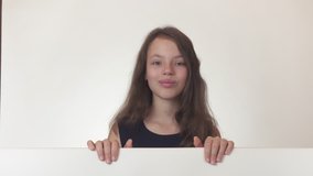 Beautiful girl teenager looks at a poster with information and happily surprised on a white background stock footage video.
